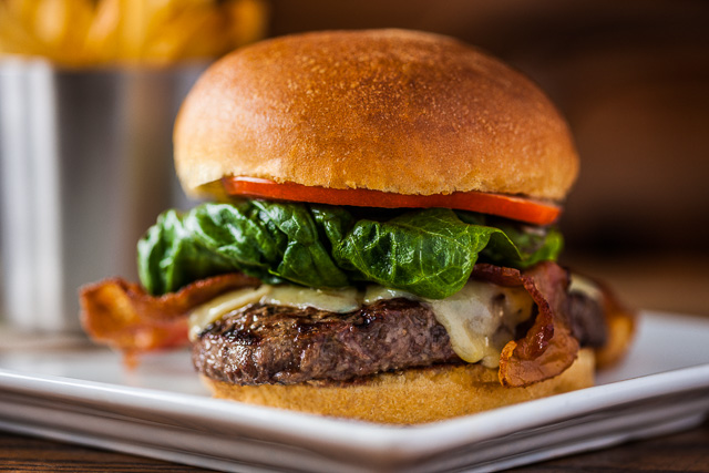 Photograph of a Juicy Hamburger with french fries in the background.