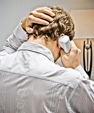 Photo of a man on the phone, shot from behind grabbing his head in frustration.