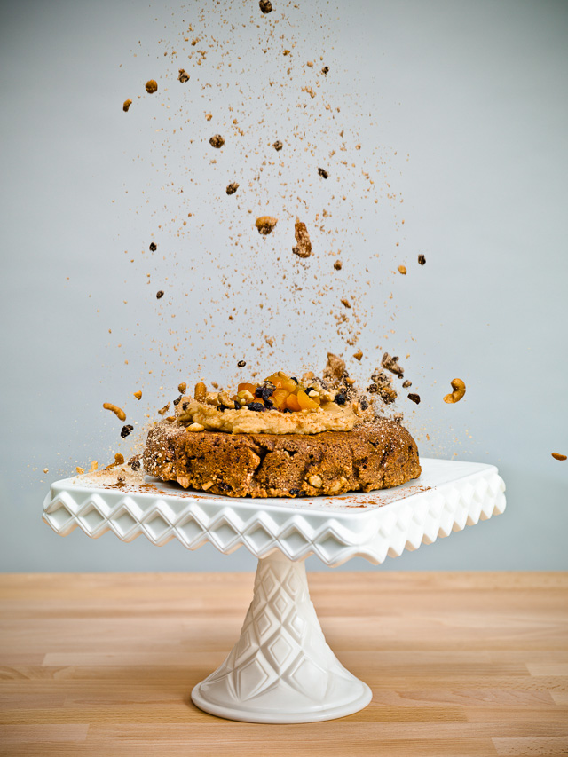 Photo of a cake on a platter with ingredients raining down on it.