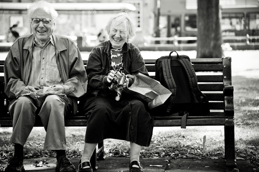 Senior Couple sitting on a bench in a park having lunch and laughing